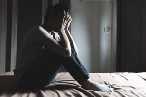 A man struggling with an underlying mental health condition and addiction cover his face in his hands in distress.