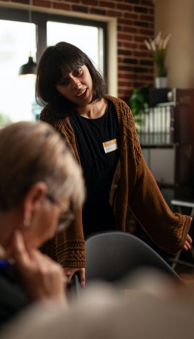 woman-smiling-and-talking-about-recovery-with-people-at-aa-therapy-meeting[1]